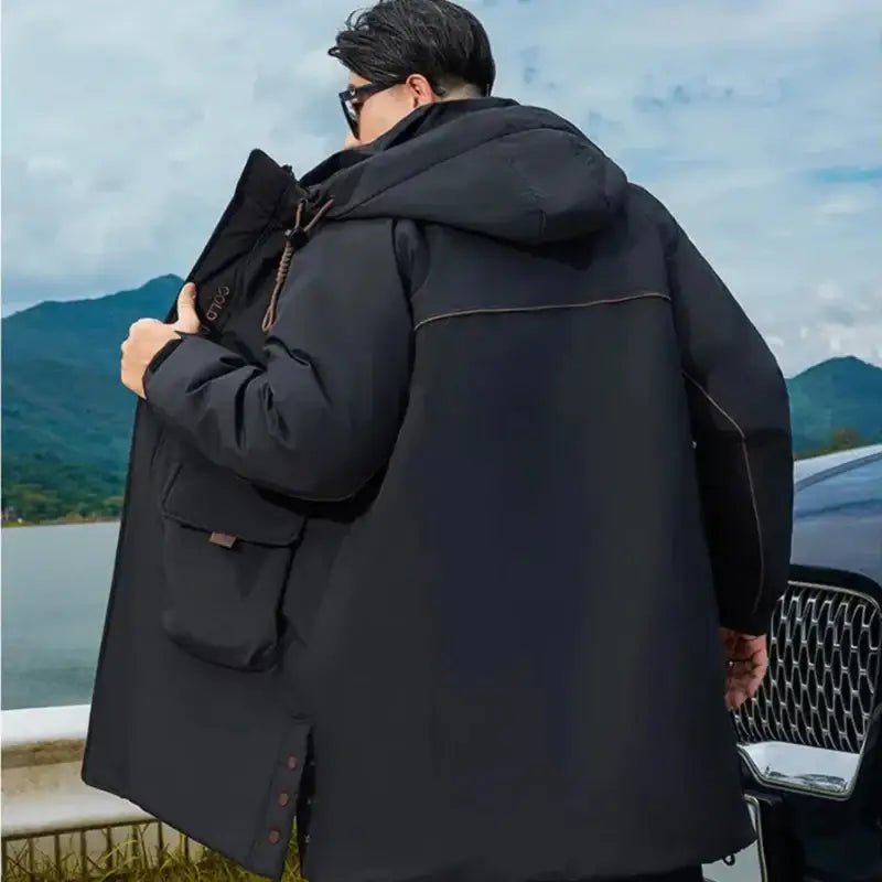 Homme portant une parka longue homme grande taille noire avec capuche, face à un paysage montagneux.