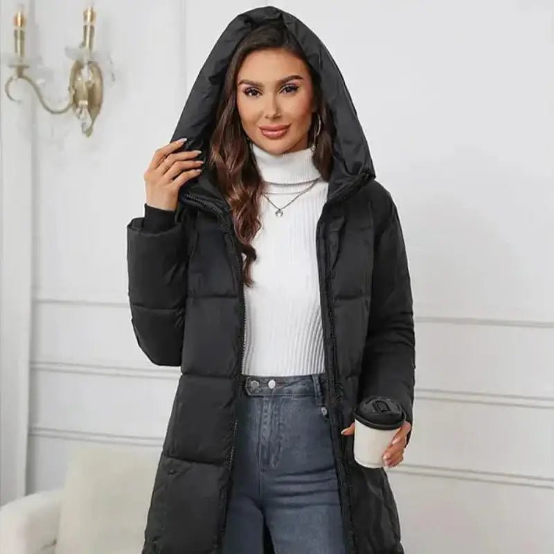 Femme portant une parka femme noire longue matelassée avec une tasse à café, devant un décor intérieur.